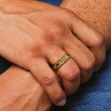 Close-up of a hand wearing a gold ring with red stones on a blue fabric background
