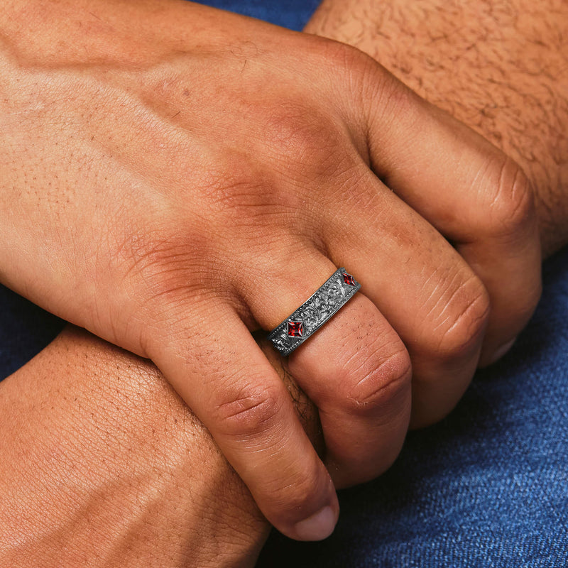 Close-up of a hand wearing a silver ring with red stones on a blue fabric background